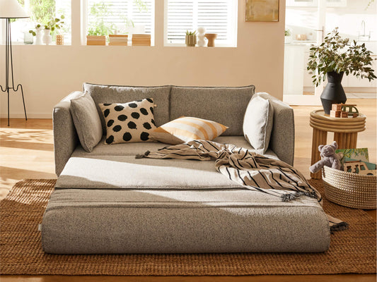 A light grey sofa with black and white polka dot and striped throw pillows, a woven rug, and a wooden side table with plants.